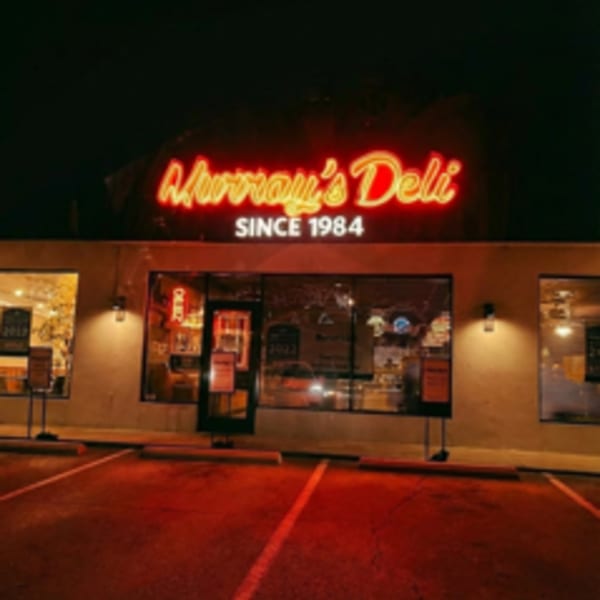 Exterior of Murray's Deli at night, with a bright red neon sign and illuminated parking lot.