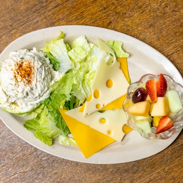 A deli plate with chicken salad, lettuce, Swiss and cheddar cheese, and a fruit cup.