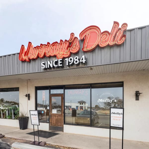 Exterior of Murray's Deli with a large red neon sign and curbside pickup signs.