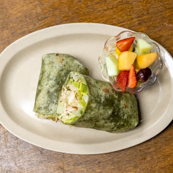 Murray's Restaurant & Deli's chicken salad wrap in a green tortilla with a side of fruit.