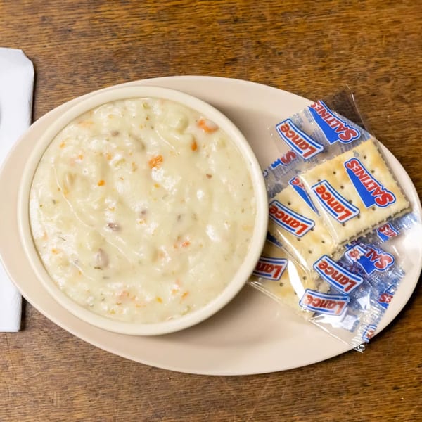 A bowl of creamy clam chowder with carrots and herbs, served with Lance Saltines crackers.