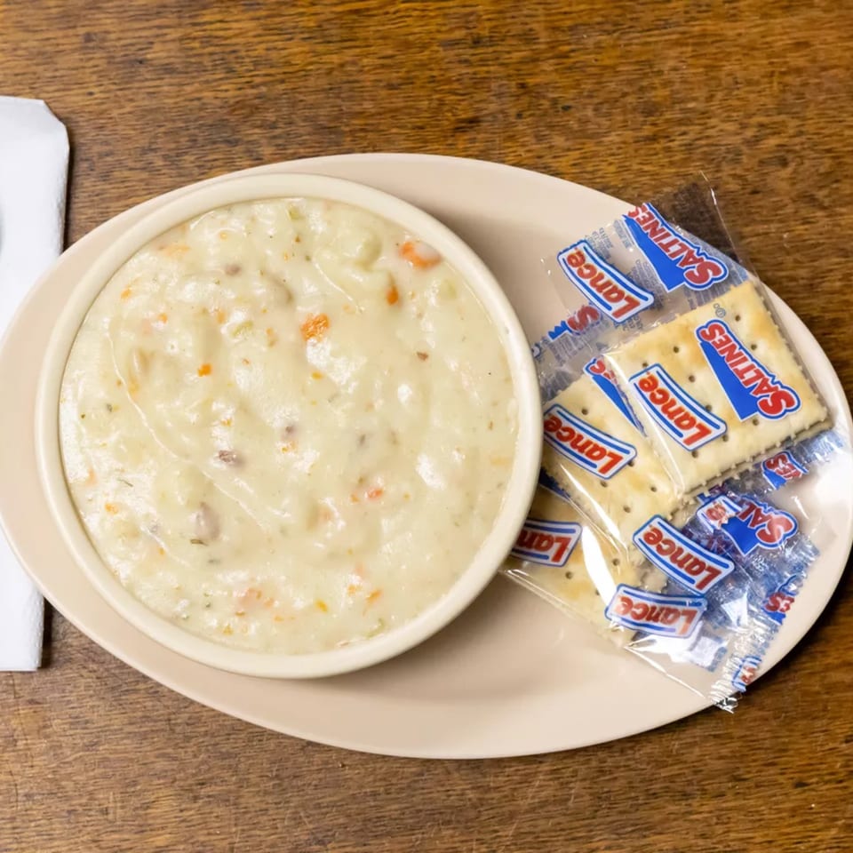 A bowl of creamy clam chowder with carrots and herbs, served with Lance Saltines crackers.